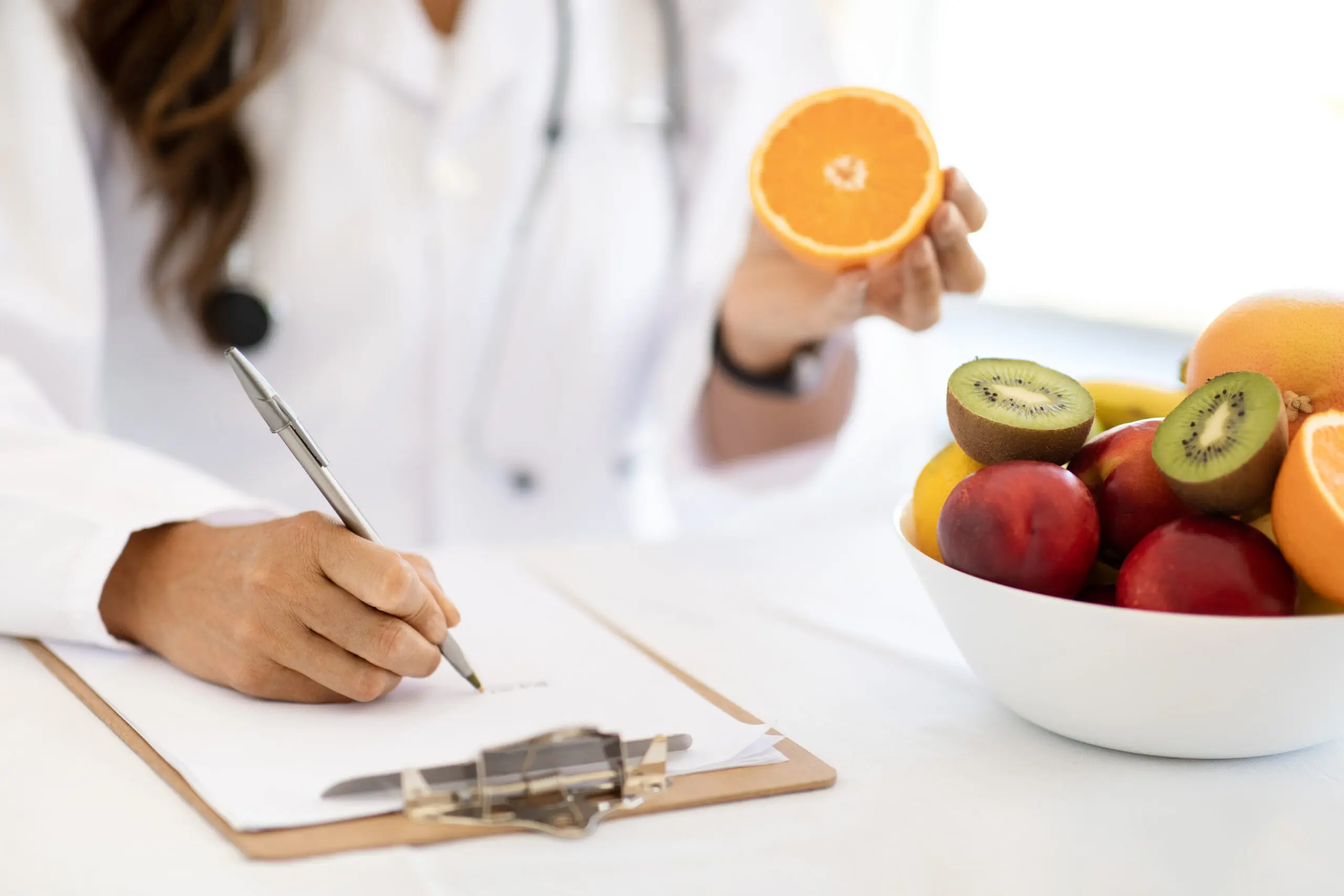A doctor holding an orange and writing on paper.