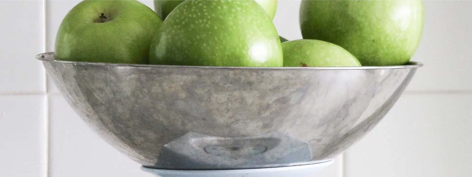 A metal bowl filled with green apples on top of a table.