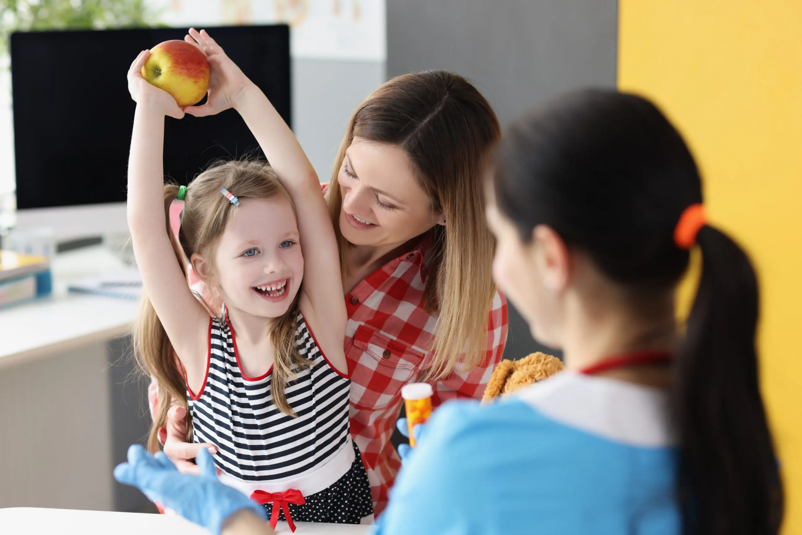 A woman and girl holding an apple in the air.