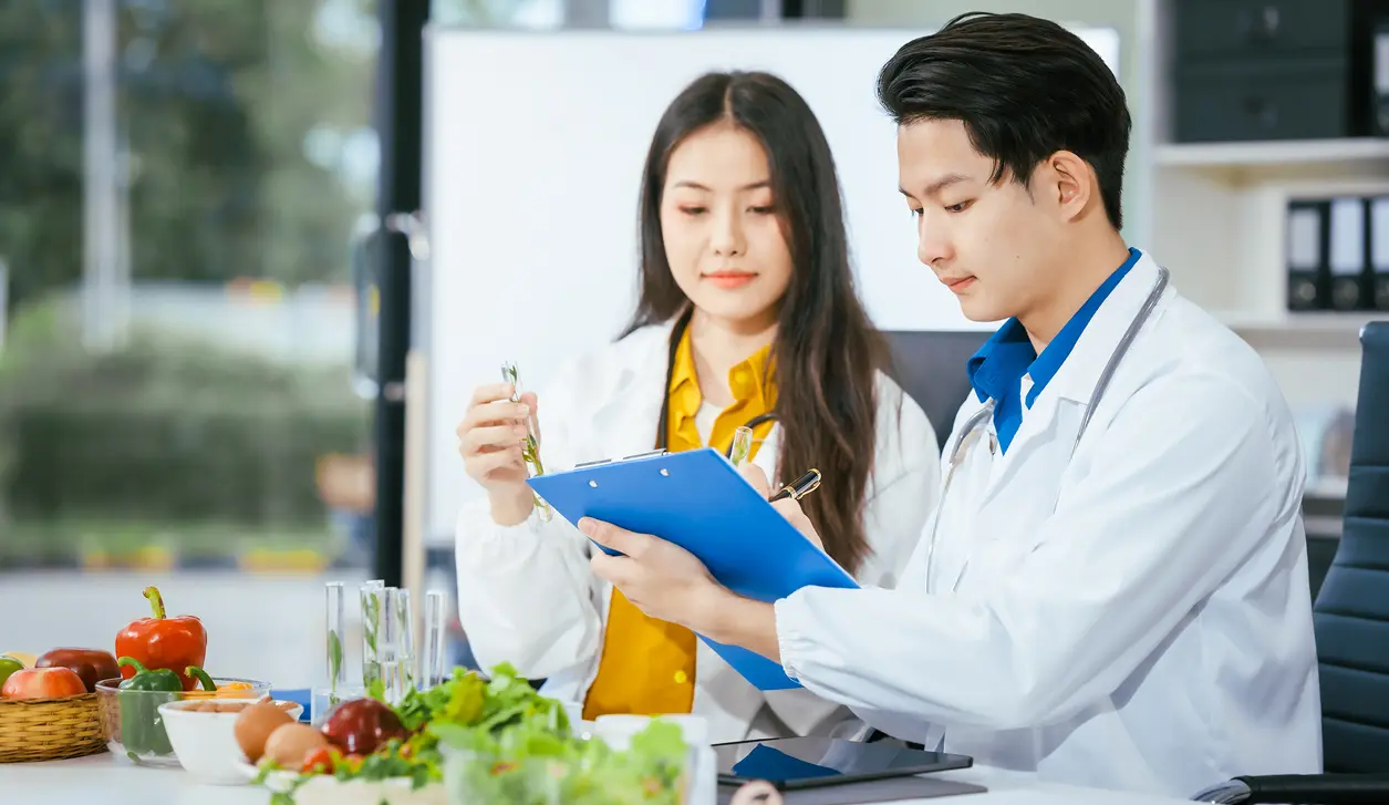A man and woman in lab coats looking at a clipboard.