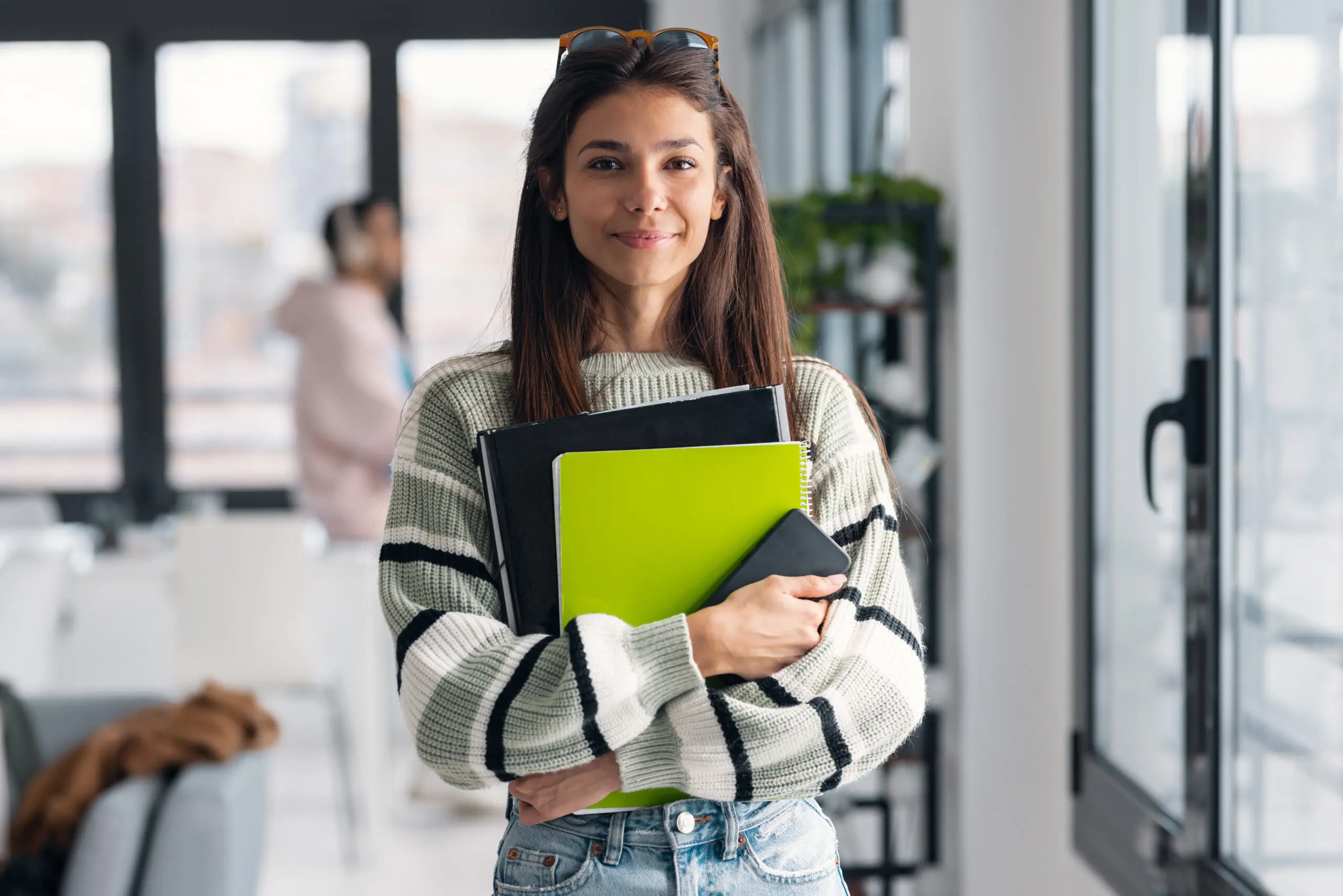 Attractive young designer woman holding some folders and smartphone while looking at camera in a modern office A woman holding two notebooks and smiling for the camera.